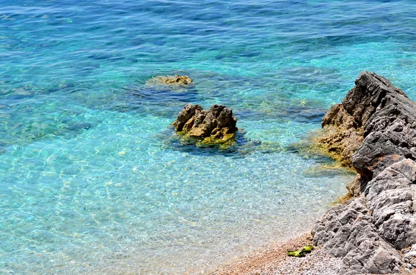 Rotsachtig strand met helder blauw water — Stockfoto