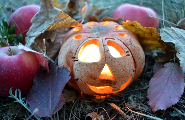 Свеча тыква с горящей свечой внутри, среди осенних опавших листьев и красных яблок, символ Хэллоуина — стоковое фото