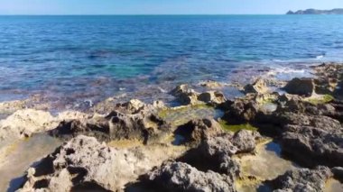 Dalgaların denize vurduğu kayalık bir sahilden kamera hareketi. Arka planda bir pelerin ile