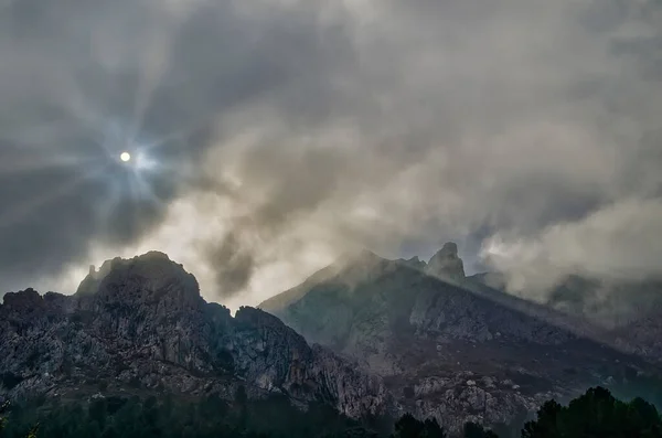 Low clouds covering the peaks of a mountain. The beams of the sun goes trough the clouds.