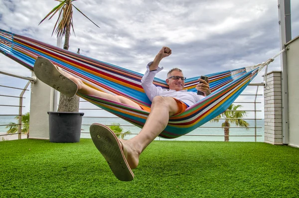 Telecommuter receiving good news by the smartphone while lying in a hammock in a balcony by the sea