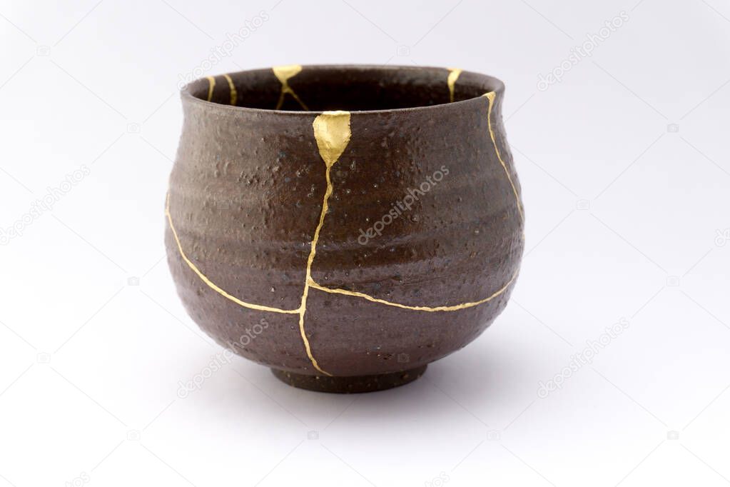 Kintsugi brown tea ceremony tea cup. Gold cracks restoration on old Japanese ceramic.