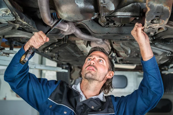 Mechanic repairing a lifted car wit — Stock Photo, Image