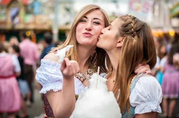 Twee jonge vrouwen in Dirndl jurk of klederdracht, kussen met cotton candy floss op het Oktoberfest Rechtenvrije Stockfoto's