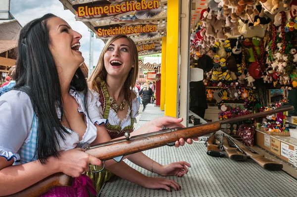 Twee mooie meisjes spelen schieten Spelletjes en plezier op Duitse kermis Oktoberfest. Het dragen van traditionele Dirndl jurken. Stockfoto