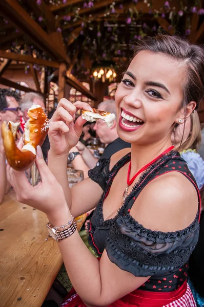 Mooie jonge vrouw in traditionele Dirndl Oktoberfest Pretzel, multiraciale Aziatisch, eten uit de Filippijnen en Kaukasische mix Stockafbeelding