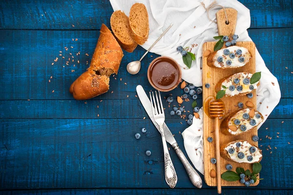 Sanduíches com queijo macio e mirtilos em um fundo de madeira. Um pequeno-almoço saudável — Fotografia de Stock