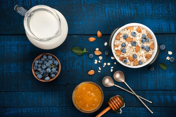 Petit déjeuner sain sur fond de bois bleu foncé : flocons d'avoine, lait, bleuets, miel et amandes. Style rustique . — Photo