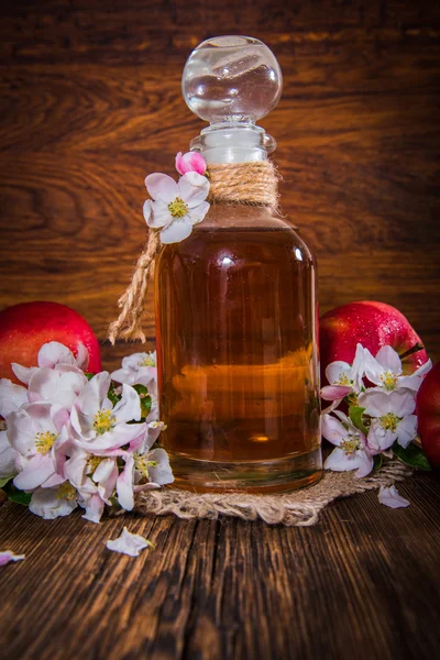 Een fles van appel cider azijn (cider), verse appels en appelboom bloemen op een houten achtergrond. Landelijke stijl. — Stockfoto