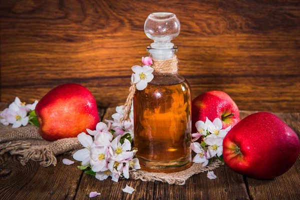 Een fles van appel cider azijn (cider), verse appels en appelboom bloemen op een houten achtergrond. Landelijke stijl. — Stockfoto
