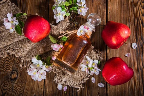 Uma garrafa de vinagre de maçã (cidra), maçãs frescas e flores de macieira em um fundo de madeira. Estilo de país . — Fotografia de Stock