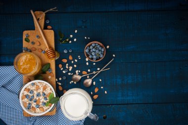 Koyu mavi ahşap arka plan üzerinde sağlıklı bir kahvaltı: yulaf ezmesi, süt, yaban mersini, bal ve badem. Rustik tarzı.