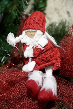 Noel süsü. Kırmızı elbiseli yün bebek kırmızı bir rafya kurdelesinde oturuyor. 