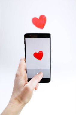 Kırmızı ahşap bir kalbin akıllı telefonuyla fotoğraf çeken kadın.