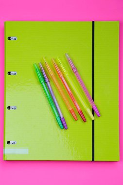 Pembe ve yeşil arkaplana karşı çeşitli renkli kalemlere sahip bir dizinin üst görünümü