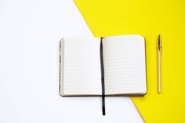 Açık bir defterin üst görüntüsü, altın renkli bir kalem beyaz ve sarı bir arka grup.