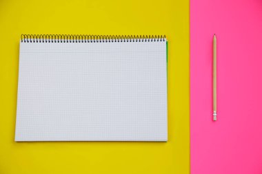 Sarı ve pembe arka plana karşı açık bir defterin ve bir kalemin üst görünümü
