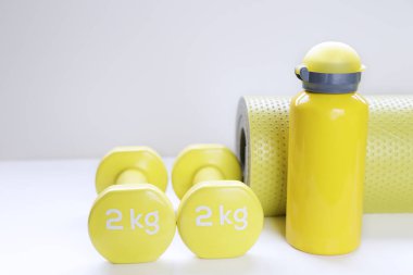 Sarı halterler, paspas ve su şişesi tarafsız arkaplanda. Fitness Konsepti.