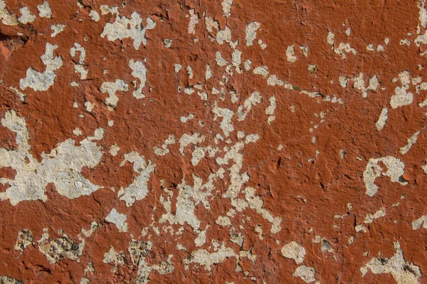 The texture of a concrete wall with crumbling orange paint.