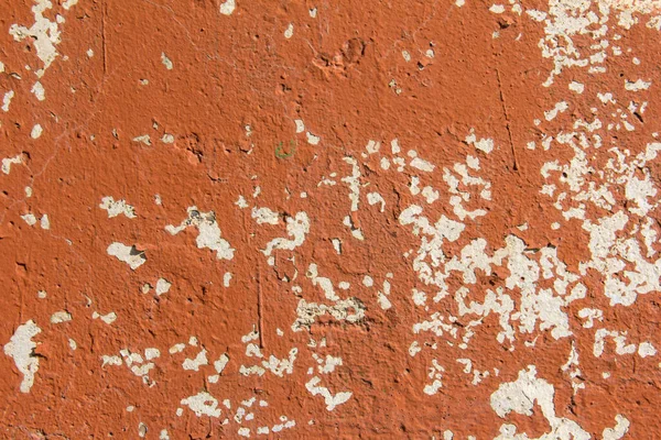 The texture of a concrete wall with crumbling orange paint.