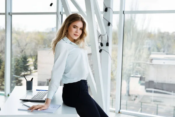 Mola sırasında parlak, modern bir ofiste kameraya bakan başarılı genç bir kadın. İş konsepti. 