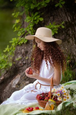 Çiçek açan bir meyveyle piknikte hasır şapkalı tatlı kırmızı kız.