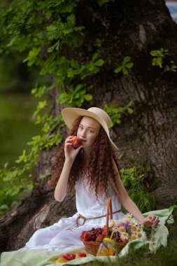 Çiçek açan bir meyveyle piknikte hasır şapkalı tatlı kırmızı kız.
