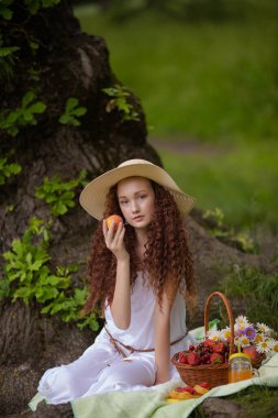 Çiçek açan bir meyveyle piknikte hasır şapkalı tatlı kırmızı kız.