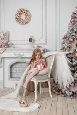 Stüdyoda, Noel ağacının yanında, sarı saçlı, melek kanatlı ve Noel topları olan küçük tatlı bir kız.