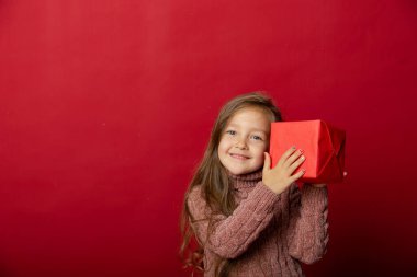 Stüdyoda kırmızı arka planda Noel oyuncaklarıyla küçük şirin bir kız