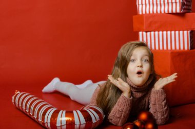 Stüdyoda kırmızı arka planda Noel oyuncaklarıyla küçük şirin bir kız