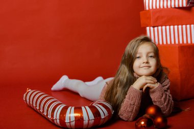 Stüdyoda kırmızı arka planda Noel oyuncaklarıyla küçük şirin bir kız