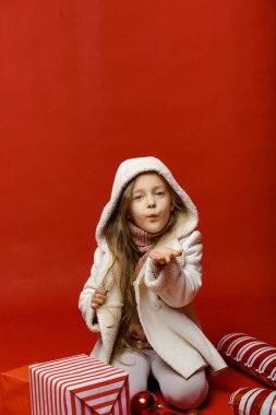 Stüdyoda kırmızı arka planda Noel oyuncaklarıyla küçük şirin bir kız