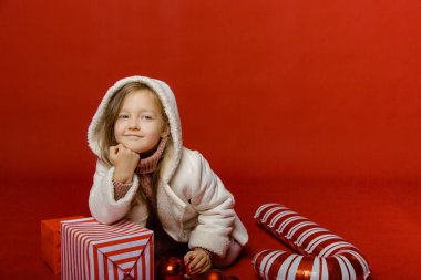 Stüdyoda kırmızı arka planda Noel oyuncaklarıyla küçük şirin bir kız