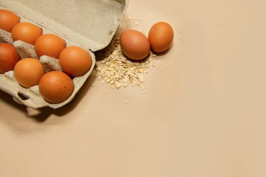 Bej bir zemin üzerinde tavuk yumurtası ve yulaf ezmesi. Yazı, sağlıklı yiyecekler, doğal ambalaj, ekoloji, yiyecek, sağlıklı yiyecekler.