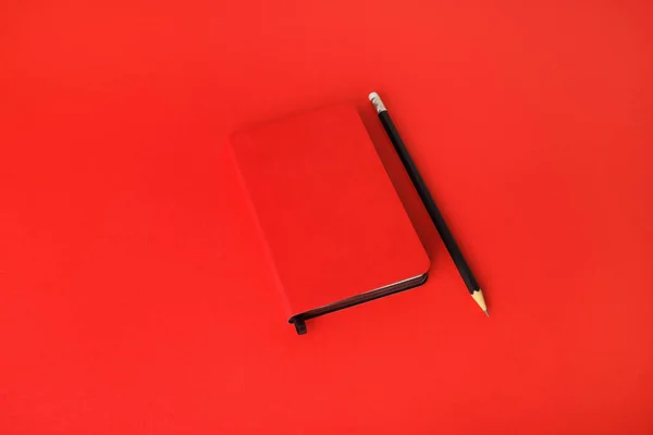 Red notebook and pencil on red paper background. Template for branding identity.