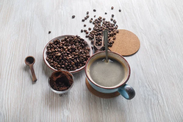 Still life with coffee cup, roasted coffee beans and ground powder on light wooden kitchen table background.