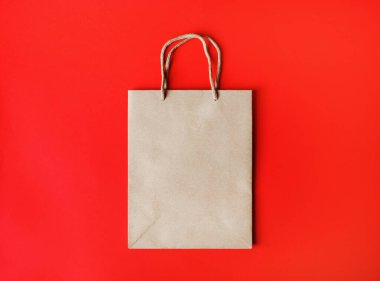 Kırmızı kağıdın arka planında ip saplı boş kahverengi bir kese kağıdı. Üst Manzara. Düz yatıyordu.