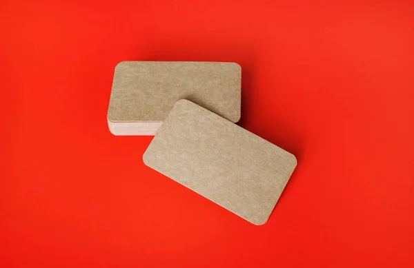 Blank kraft business cards on red paper background. Mockup for branding identity.