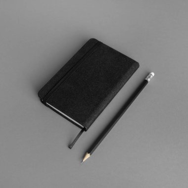 Gri kağıt arka planda boş siyah not defteri ve kalem.