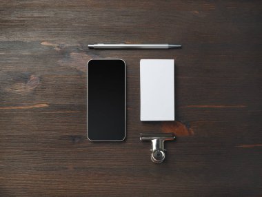 Ahşap arka planda akıllı telefon ve kırtasiye malzemeleri. Boş kartvizit, kalem ve cep telefonu. Üst Manzara. Düz yatıyordu.