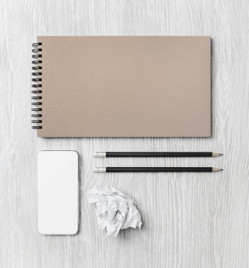 Boş ahşap masa arkaplanındaki kurumsal kimlik şablonu. Defter, akıllı telefon, kalemler ve buruşuk kağıt. Düz yatıyordu.