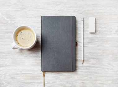 Boş defter, kalem, silgi ve açık ahşap arka planda kahve fincanı. Tepkili tasarım şablonu. Üst Manzara. Düz yatıyordu.