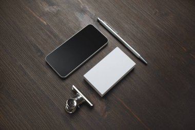 Akıllı telefon, boş kartvizit ve tahta arka planda kalem. Boş kırtasiye seti. Marka kimliği için model.