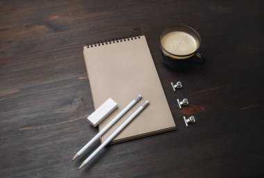 Boş kırtasiye şablonu. Boş Kraft defteri, kahve fincanı, tahta masa arkasındaki kalem ve silgi..