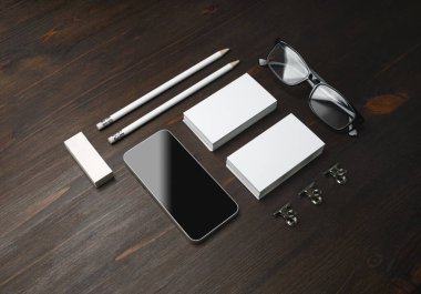 Akıllı telefon ve boş kağıtlar: kartvizitler, kalemler, silgi ve tahta masa arkasındaki gözlükler.
