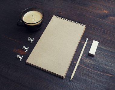 Kırtasiye modeli. Boş Kraft not defteri, kalem, silgi ve ahşap masa arkasındaki kahve fincanı..