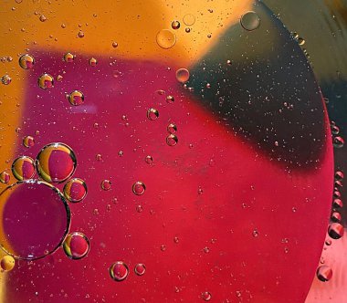 yüzen yağ damlaları farklı renklerde parıldıyor ve renkli bir arkaplanda hava kabarcıklarının yanında şekilleniyor.