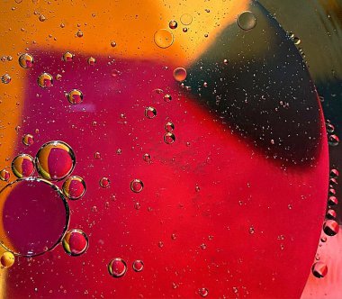 yüzen yağ damlaları farklı renklerde parıldıyor ve renkli bir arkaplanda hava kabarcıklarının yanında şekilleniyor.