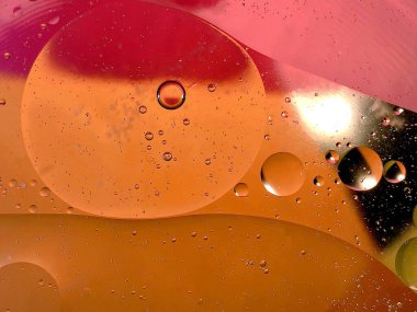 yüzen yağ damlaları farklı renklerde parıldıyor ve renkli bir arkaplanda hava kabarcıklarının yanında şekilleniyor.